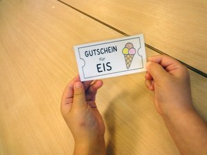 Ein Kind hält einen selbst gestalteten Eisgutschein mit einer bunten Eiswaffel in den Händen. Der Gutschein wurde für eine Eisaktion der Elefantengruppe in der DiKiTa zum Start der Sommerferien gestaltet.