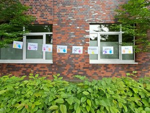 Backsteingebäude der DiKiTa mit einer von Kindern gestalteten Girlande in den Fenstern. Die Schilder informieren darüber, dass ab August noch Krippenplätze frei sind.
