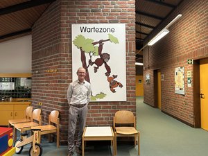 Dr. Michael Wagner steht lächelnd im Wartebereich des Sozialpädiatrischen Zentrums vor einem Wandbild mit zwei Orang-Utans und dem Schriftzug „Wartezone“.