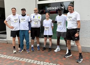 Sechs Mitglieder des Lauf-Teams der Fachklinik Weser-Ems posieren vor ihrer Teilnahme am Everstener Brunnenlauf für ein Gruppenfoto. Sie tragen weiße Laufshirts mit Startnummern und wirken motiviert und gut gelaunt.