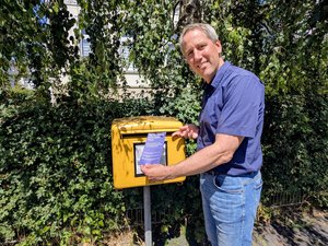Mario Behrends, Vorstand der Diakonie im Oldenburger Land, wirft eine blaue Aktionspostkarte der Diakonie Deutschland in einen gelben Briefkasten ein. Die Aufnahme entstand an einem sonnigen Tag vor einem großen Baum und verdeutlicht die Beteiligung an der bundesweiten Protestaktion gegen geplante Kürzungen in der Kinder-, Jugend- und Eingliederungshilfe.