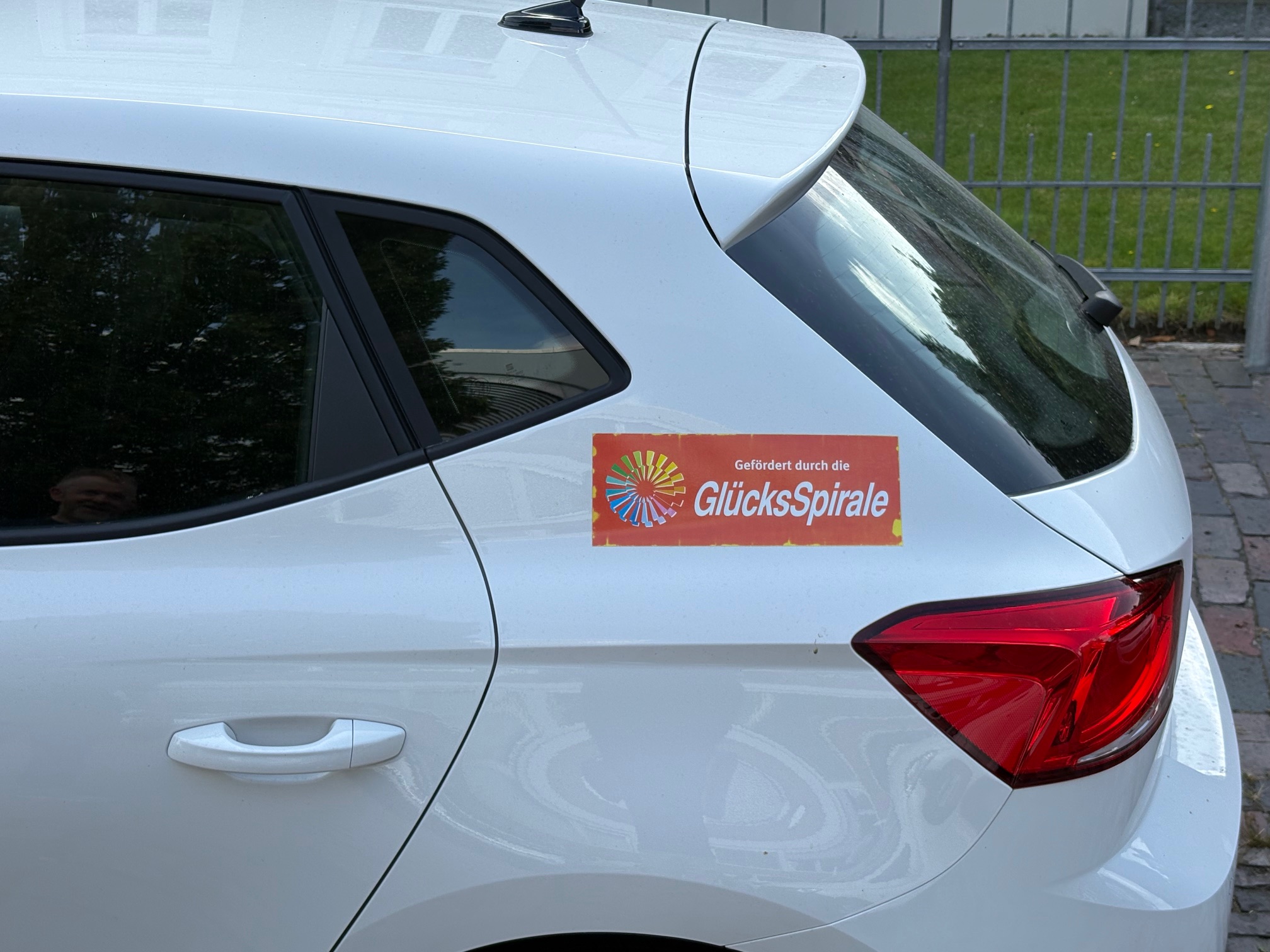 Detailaufnahme des neuen Dienstwagens der Ambulanten Wohnungslosenhilfe im Landkreis Friesland: Auf der Seite des weißen SEAT Ibiza ist ein Aufkleber mit dem Hinweis „Gefördert durch die GlücksSpirale“ zu sehen.