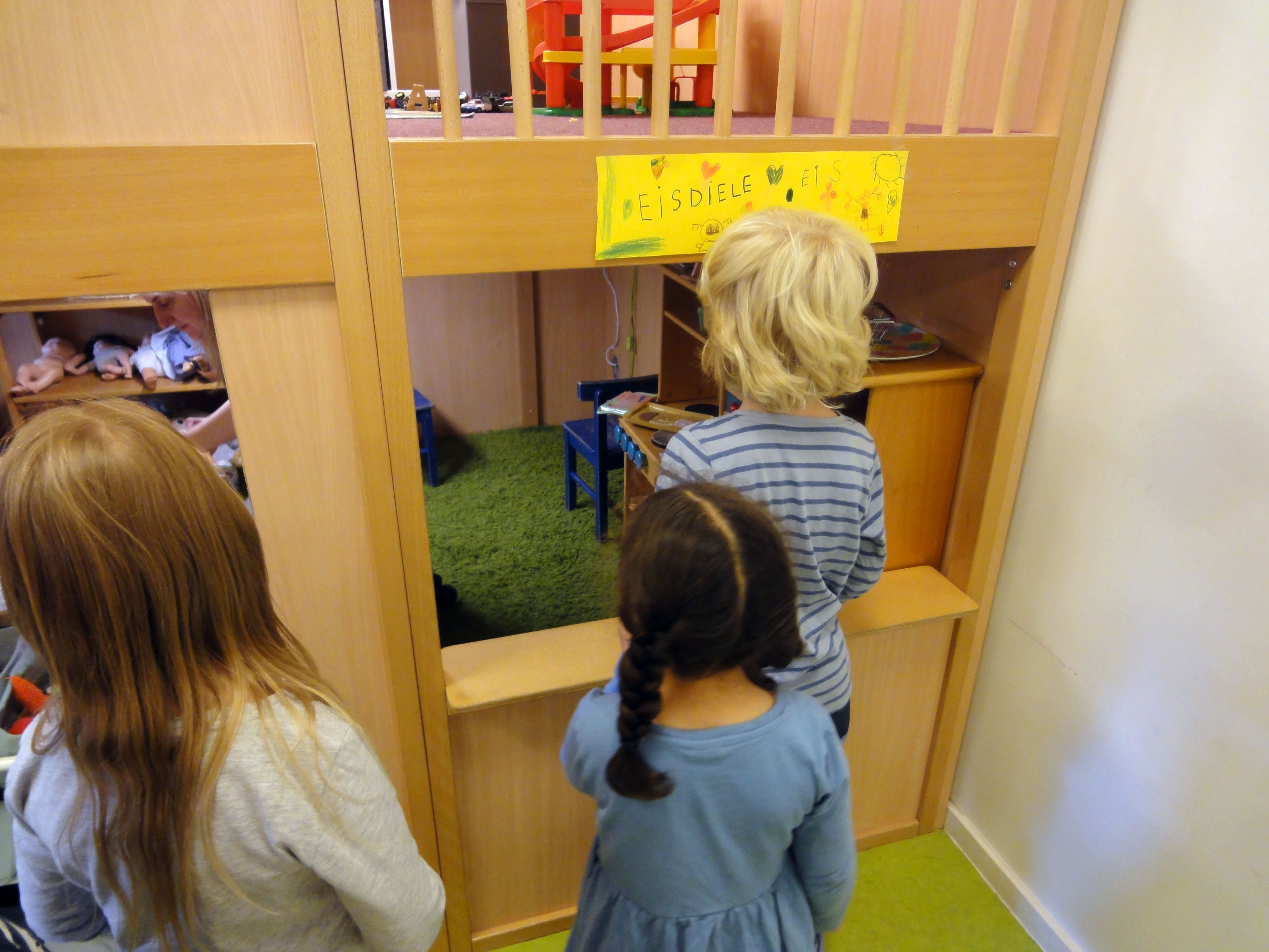 Mehrere Kinder stehen vor einer selbst gestalteten Eisdiele im Gruppenraum und warten mit Vorfreude darauf, ihr Eis auszuwählen.